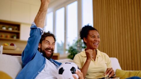 Excited couple cheering while watching soccer match at home stock photo