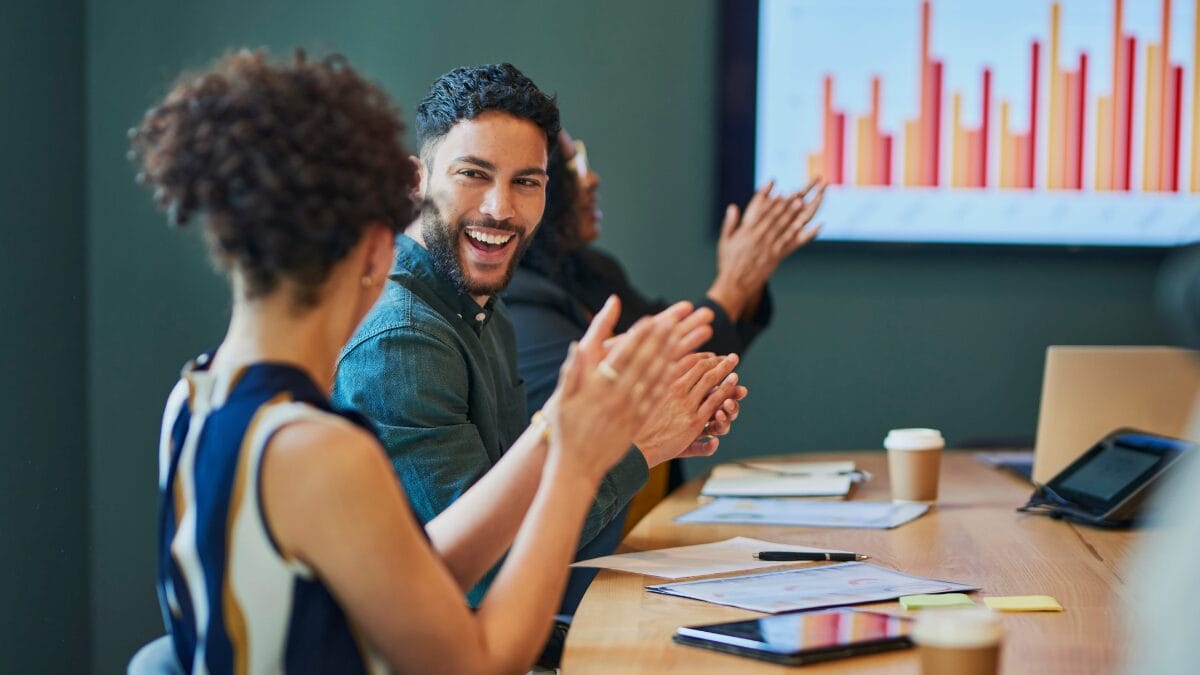Two people in a meeting smiling and clapping with data results in the background