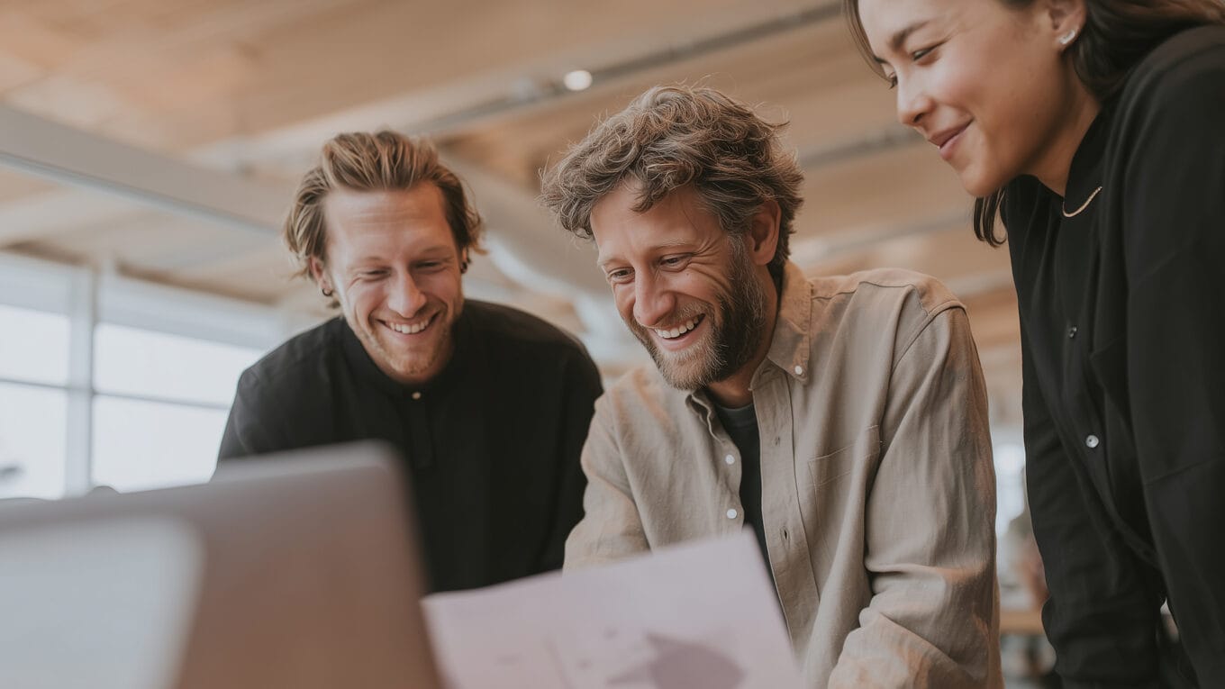 Group of three marketers smiling looking at a laptop